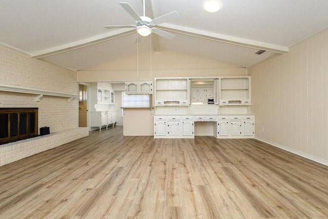 unfurnished living room featuring ceiling fan, a brick fireplace, lofted ceiling with beams, and light hardwood / wood-style flooring