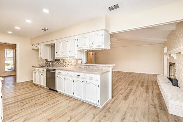 kitchen featuring white cabinets, a brick fireplace, stainless steel dishwasher, kitchen peninsula, and light wood-type flooring