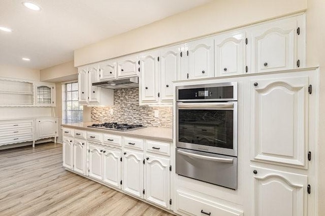 kitchen with tasteful backsplash, light wood-type flooring, white cabinets, and appliances with stainless steel finishes