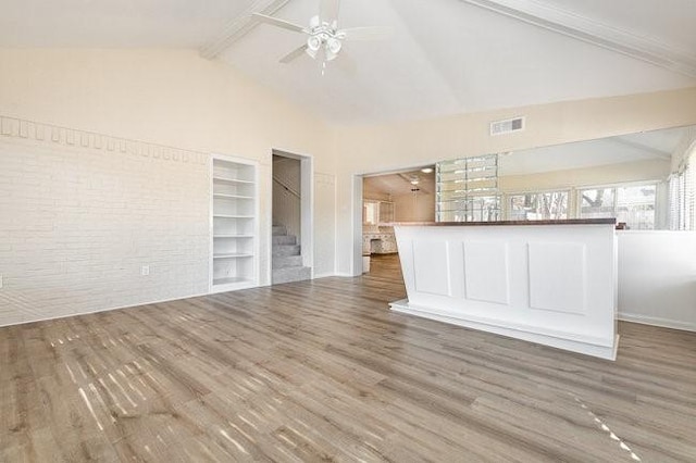 unfurnished living room with beamed ceiling, high vaulted ceiling, hardwood / wood-style flooring, ceiling fan, and brick wall