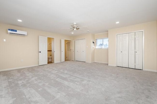 unfurnished bedroom featuring multiple closets, ceiling fan, light colored carpet, and a wall unit AC