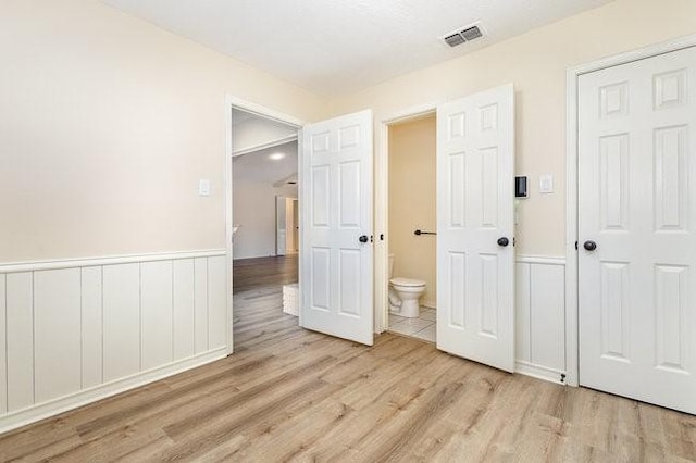 unfurnished bedroom with ensuite bathroom and light hardwood / wood-style floors