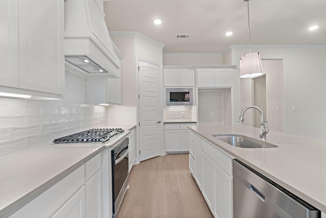 kitchen with appliances with stainless steel finishes, sink, white cabinets, hanging light fixtures, and custom range hood