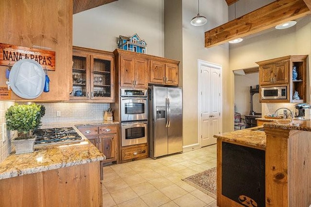 kitchen with sink, backsplash, stainless steel appliances, a high ceiling, and light stone countertops