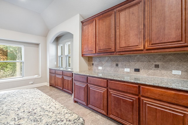 kitchen featuring light stone counters, plenty of natural light, vaulted ceiling, and tasteful backsplash