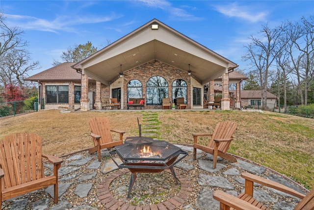 rear view of property featuring ceiling fan, a patio area, a fire pit, and a lawn