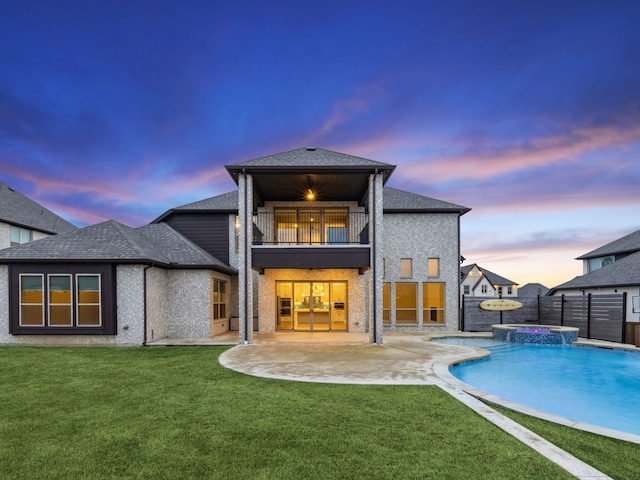 back house at dusk with a swimming pool with hot tub, a yard, a patio area, and a balcony