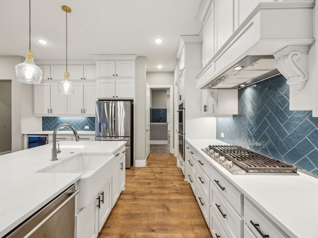 kitchen featuring sink, stainless steel appliances, white cabinets, decorative light fixtures, and light wood-type flooring