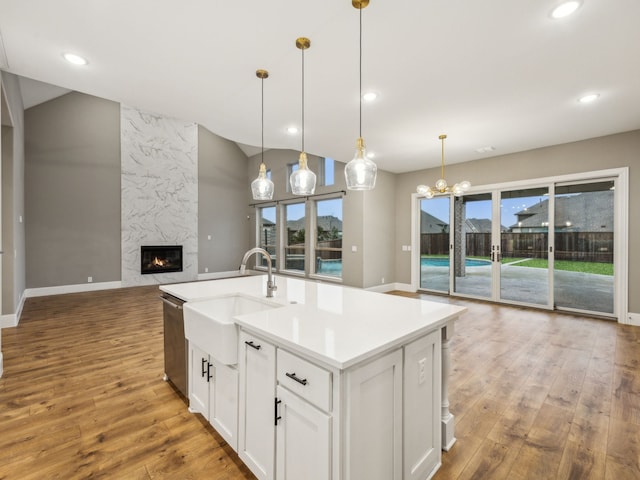 kitchen featuring pendant lighting, hardwood / wood-style flooring, a premium fireplace, white cabinetry, and an island with sink