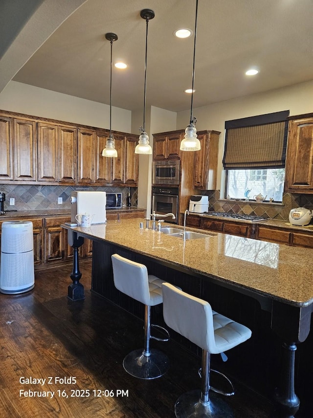 kitchen with appliances with stainless steel finishes, dark hardwood / wood-style floors, decorative light fixtures, decorative backsplash, and a center island with sink