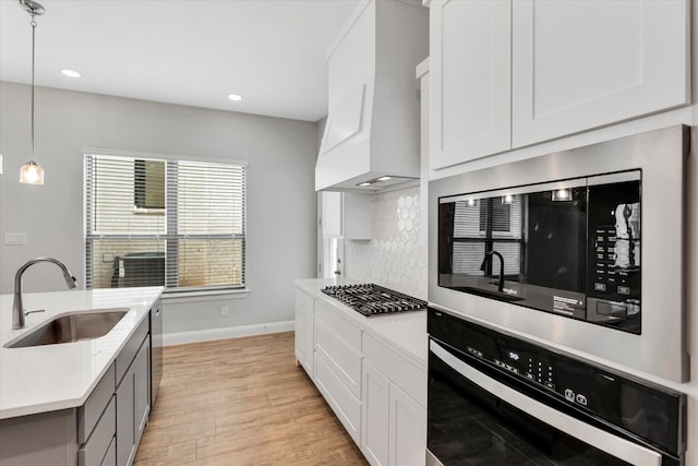 kitchen with sink, white cabinetry, hanging light fixtures, stainless steel appliances, and custom exhaust hood