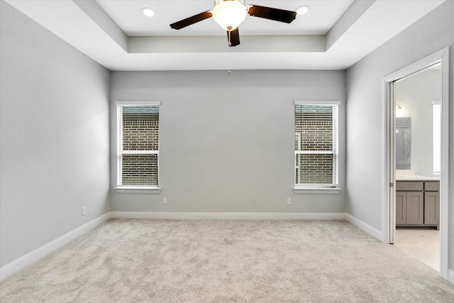 carpeted empty room with a raised ceiling and ceiling fan