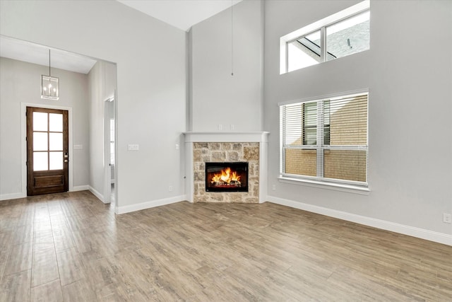 unfurnished living room featuring a high ceiling, a notable chandelier, a fireplace, and light hardwood / wood-style floors