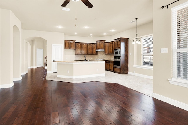 kitchen with stainless steel appliances, light countertops, an island with sink, under cabinet range hood, and ceiling fan with notable chandelier