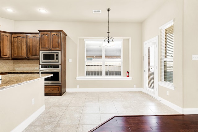 kitchen featuring light stone counters, visible vents, appliances with stainless steel finishes, tasteful backsplash, and decorative light fixtures