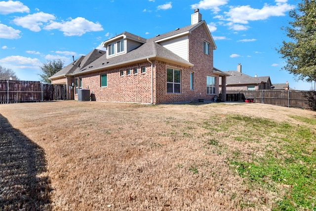 back of property featuring brick siding, a yard, a chimney, roof with shingles, and a fenced backyard