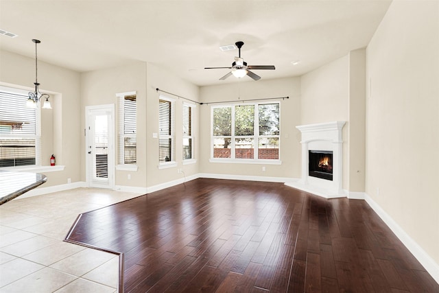 unfurnished living room featuring a lit fireplace, baseboards, wood finished floors, and ceiling fan with notable chandelier