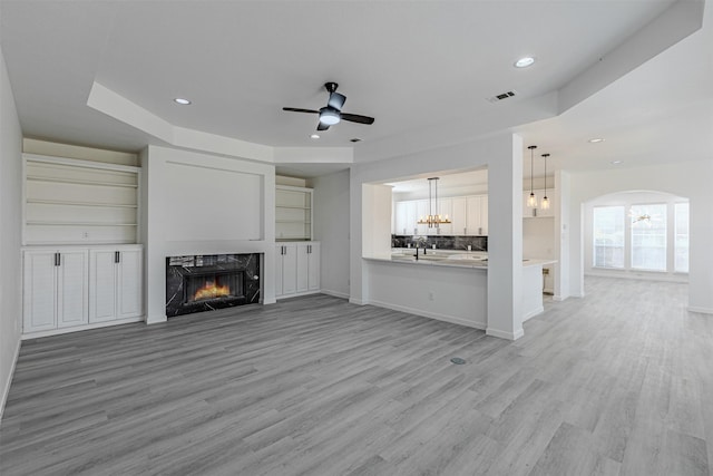 unfurnished living room featuring a fireplace, ceiling fan with notable chandelier, and light wood-type flooring