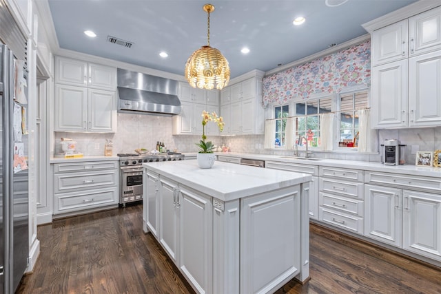 kitchen with hanging light fixtures, high end stove, white cabinets, a kitchen island, and wall chimney exhaust hood