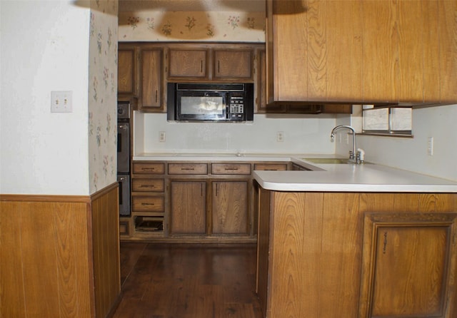 kitchen with brown cabinetry, wainscoting, double wall oven, black microwave, and a sink