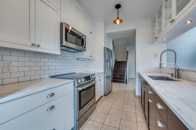 kitchen with white cabinetry, sink, hanging light fixtures, stainless steel appliances, and light stone countertops