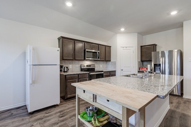 kitchen with an island with sink, dark wood-style flooring, stainless steel appliances, decorative backsplash, and dark brown cabinets