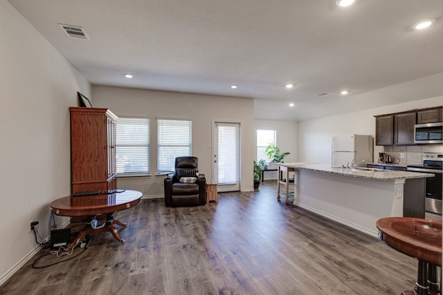 kitchen featuring visible vents, light stone countertops, dark wood finished floors, an island with sink, and stainless steel appliances