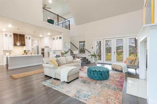 living room featuring dark wood-type flooring, a towering ceiling, ceiling fan, and french doors