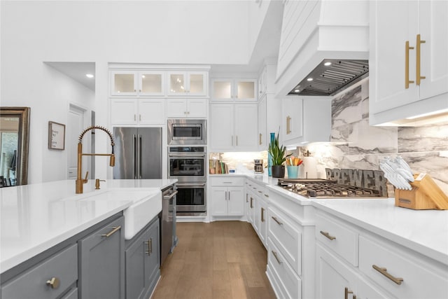 kitchen featuring appliances with stainless steel finishes, gray cabinets, premium range hood, white cabinets, and decorative backsplash