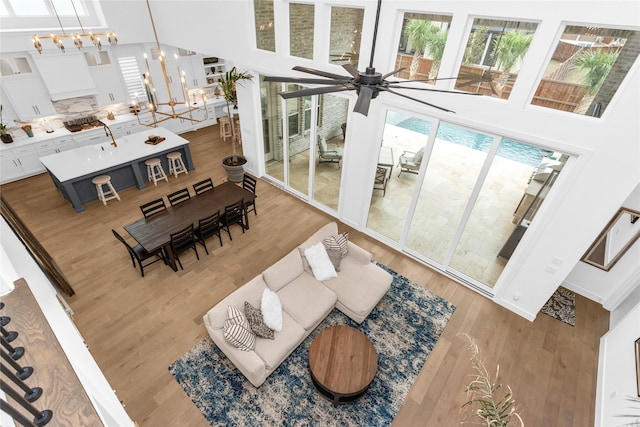 living room with hardwood / wood-style floors, ceiling fan with notable chandelier, and a towering ceiling