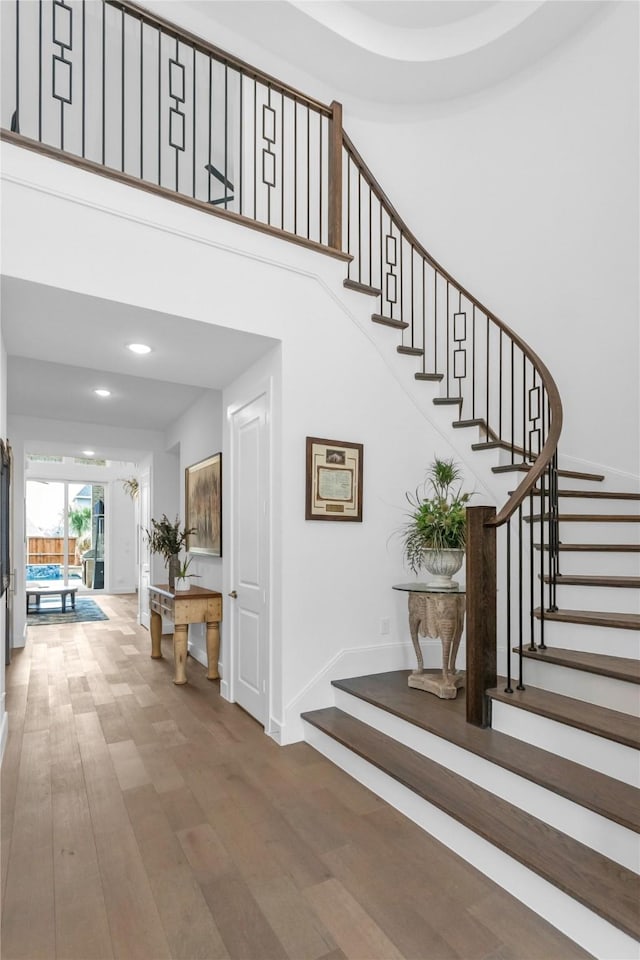 stairs featuring a towering ceiling, baseboards, wood finished floors, and recessed lighting