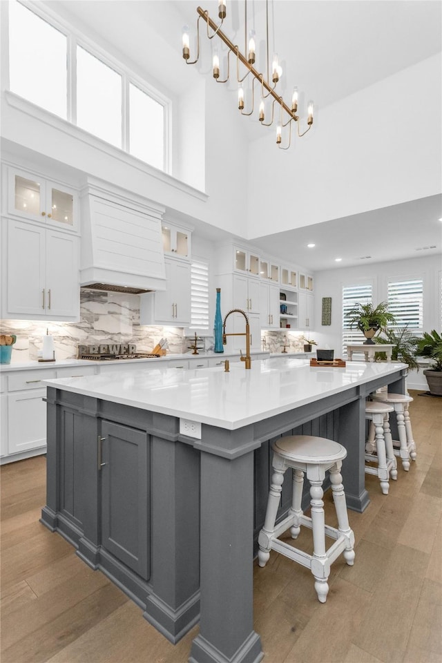 kitchen featuring a large island, white cabinets, hanging light fixtures, and custom exhaust hood