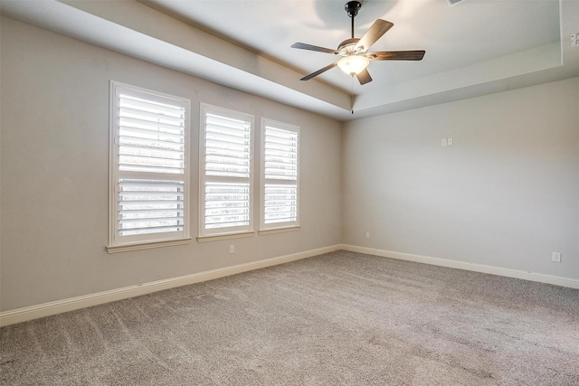 spare room with ceiling fan, a raised ceiling, and carpet