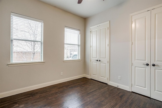 unfurnished bedroom featuring multiple closets, dark wood-type flooring, and ceiling fan