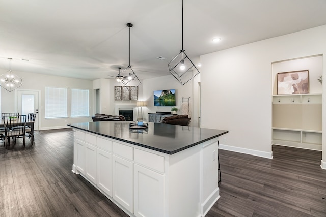 kitchen with pendant lighting, dark wood-type flooring, white cabinetry, a center island, and ceiling fan with notable chandelier