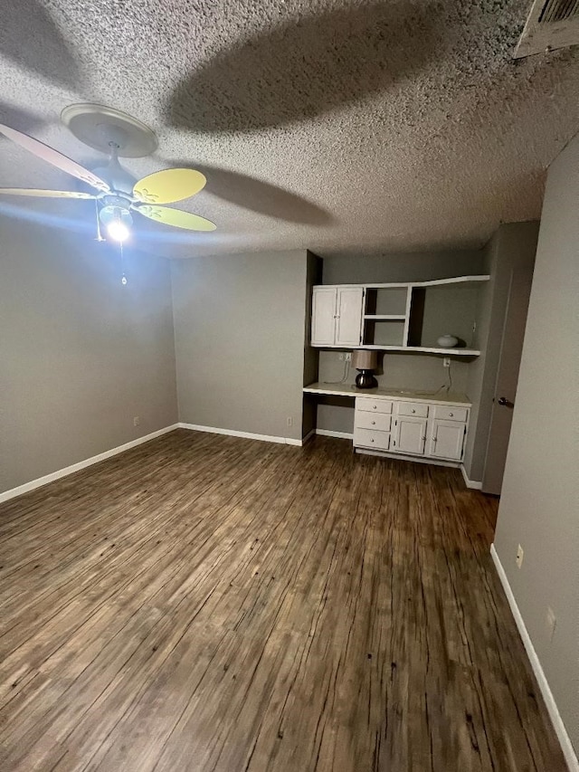 unfurnished living room with ceiling fan, dark hardwood / wood-style floors, built in desk, and a textured ceiling