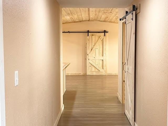 hallway featuring wood-type flooring, a barn door, wooden ceiling, and lofted ceiling