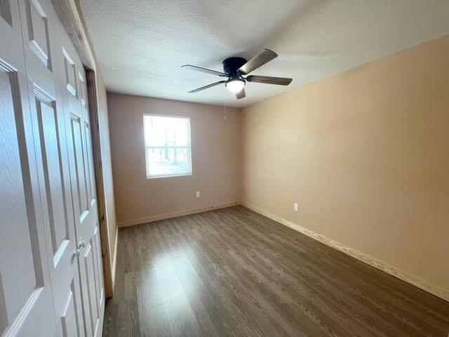 spare room with dark wood finished floors, ceiling fan, baseboards, and a textured ceiling