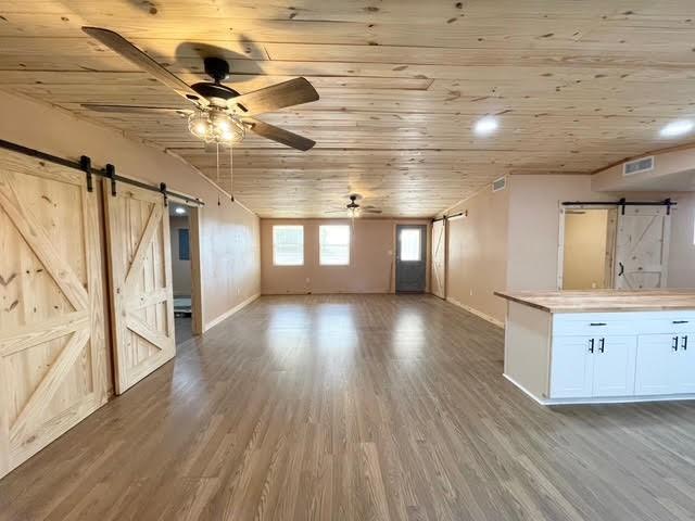 interior space featuring wood finished floors, visible vents, ceiling fan, a barn door, and wooden ceiling