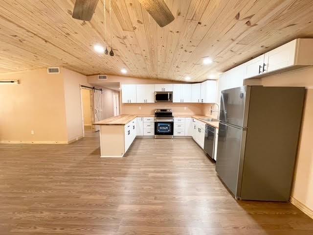 kitchen with stainless steel appliances, white cabinetry, a barn door, and wood ceiling