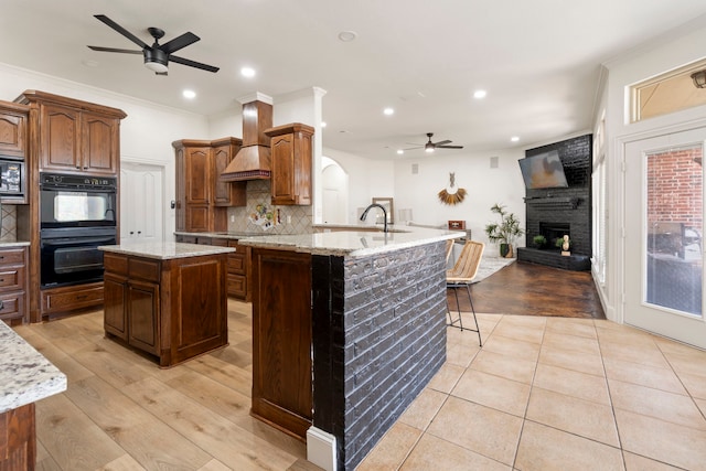 kitchen featuring a kitchen island, decorative backsplash, custom exhaust hood, black appliances, and light stone countertops