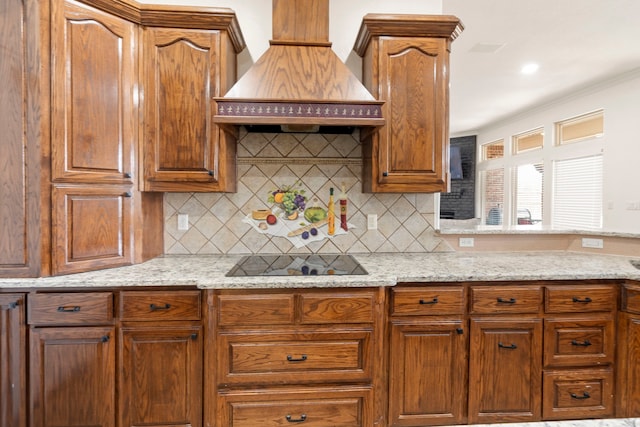 kitchen featuring light stone countertops, custom range hood, black electric stovetop, and decorative backsplash