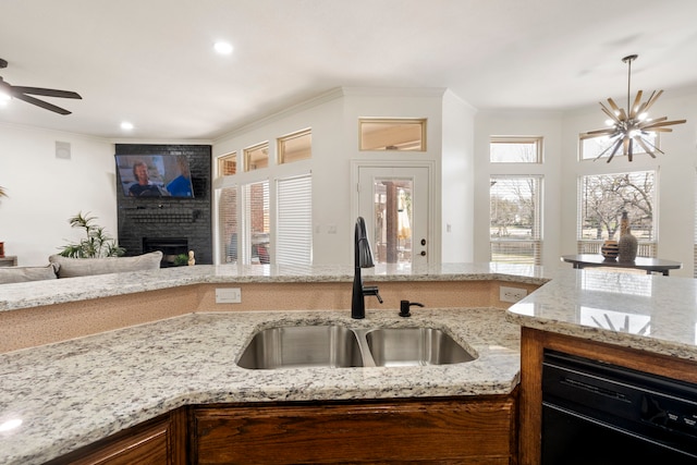 kitchen with sink, light stone counters, a brick fireplace, ornamental molding, and ceiling fan with notable chandelier