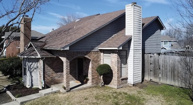 exterior space with a shingled roof, a lawn, a chimney, fence, and brick siding