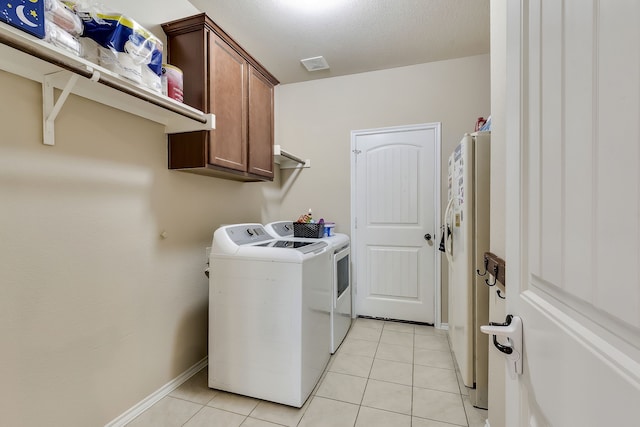 washroom with light tile patterned floors, a textured ceiling, cabinets, and washing machine and clothes dryer