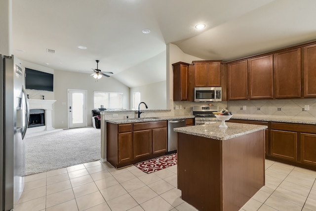 kitchen featuring sink, appliances with stainless steel finishes, a kitchen island, vaulted ceiling, and light colored carpet