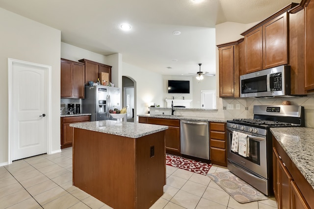 kitchen with sink, appliances with stainless steel finishes, a center island, light stone counters, and tasteful backsplash