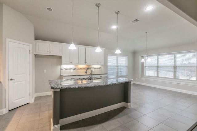 kitchen featuring tasteful backsplash, light stone countertops, decorative light fixtures, sink, and white cabinetry