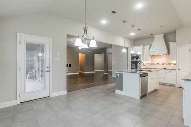 kitchen with appliances with stainless steel finishes, pendant lighting, a kitchen island with sink, and premium range hood