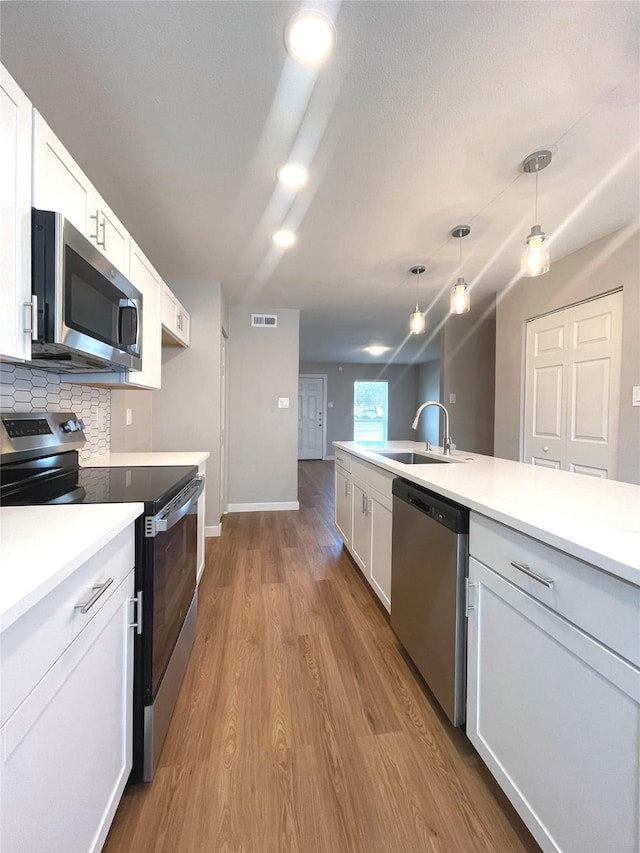 kitchen featuring visible vents, appliances with stainless steel finishes, wood finished floors, a sink, and backsplash